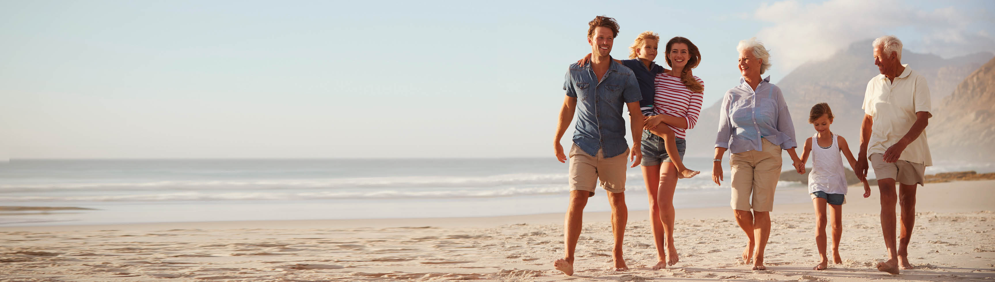 Multi Generation Family On Vacation Walking Along Beach Together