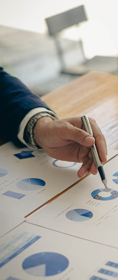 Businessman holding pen pointing to marketing graph and working on the laptop computer, working online and analyzing vertical picture financial documents.