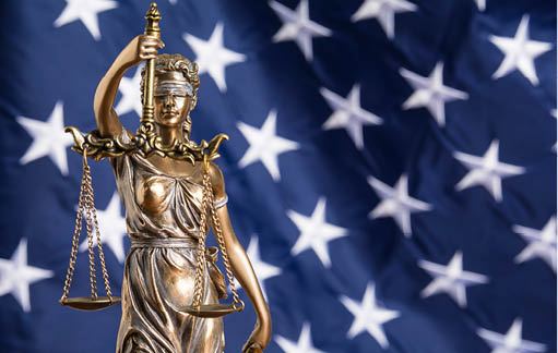 The statue of justice Themis or Justitia, the blindfolded goddess of justice against a flag of the United States of America, as a legal concept