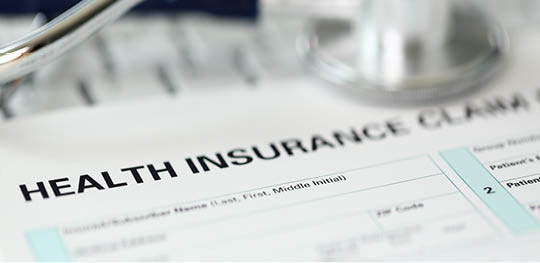 Letterbox view of stethoscope head and silver pen lying on application form at insurance agent worktable in company office closeup
