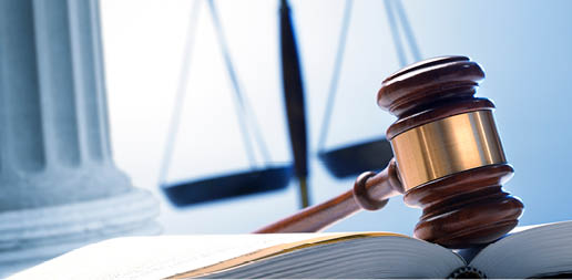 A gavel rests on top of an open law book with a justice scale and a Greek column in the background.